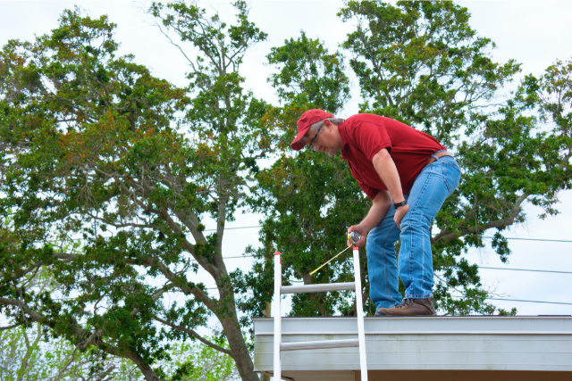 Roof inspection by worker on a ladder with measuring tape
